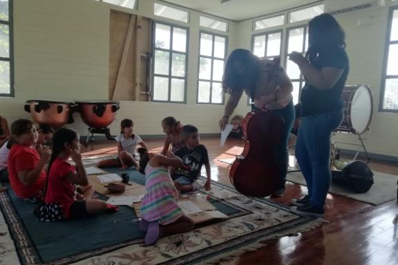 Niñas y niños se preparan para dar inicio a una clase de cello con dos maestras