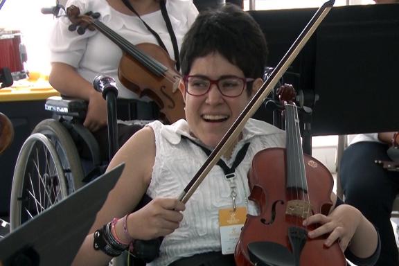 Adolescente violinista en silla de ruedas sonríe durante un concierto